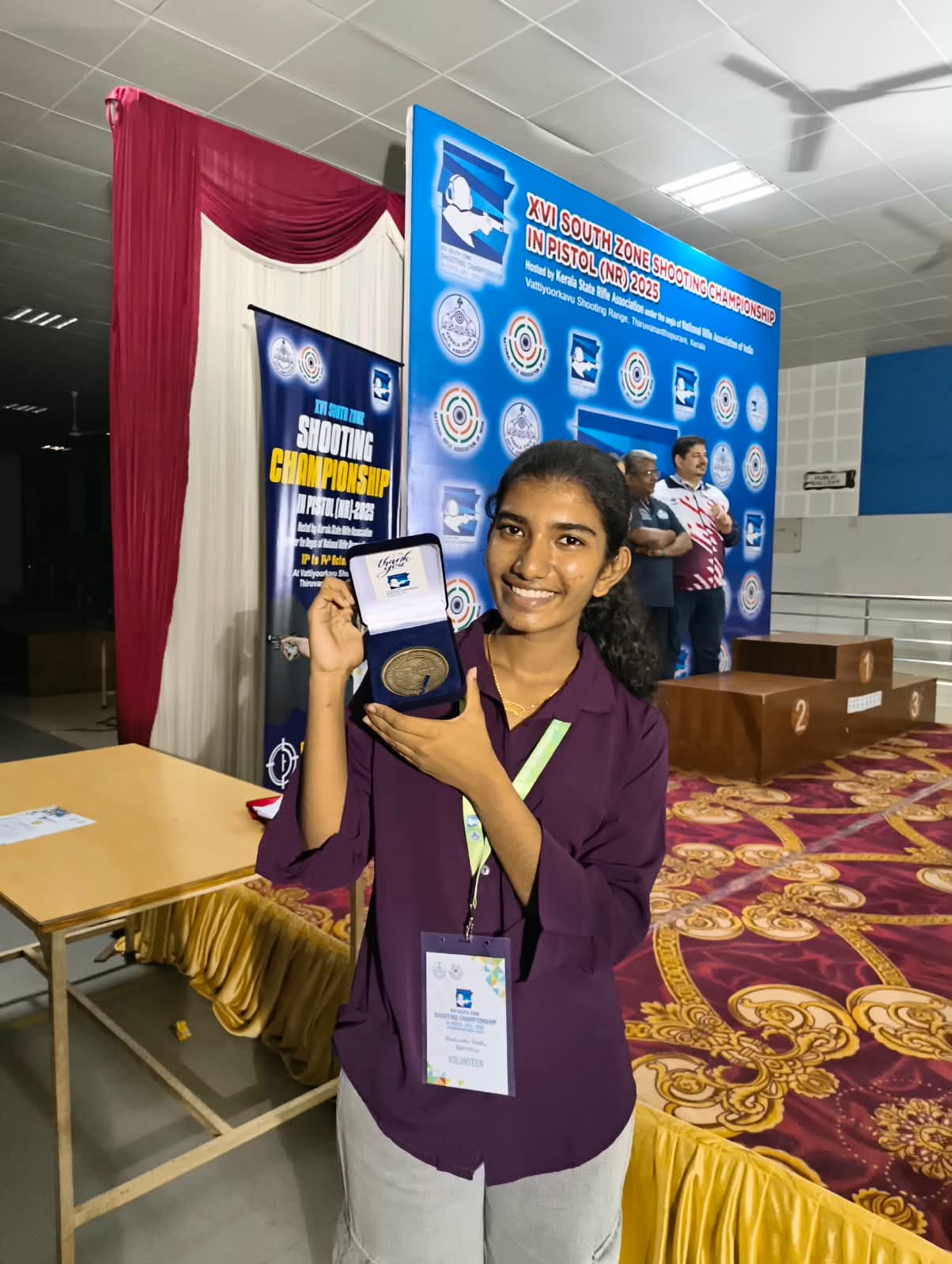 Brahmitha G wearing a volunteer badge and holding a memento at the South Zone pistol championship